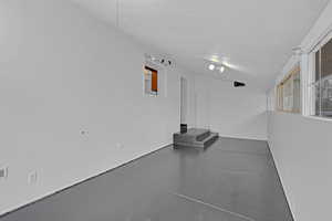 Spare room featuring concrete flooring, vaulted ceiling, and a textured ceiling