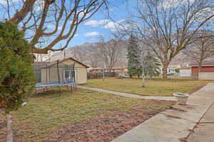 View of yard featuring a trampoline, fence, a mountain view, and an outbuilding