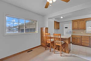 Kitchen with baseboards, visible vents, brown cabinets, light countertops, and a kitchen bar
