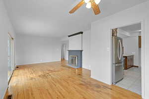 Unfurnished living room with visible vents, baseboards, ceiling fan, light wood-type flooring, and a brick fireplace