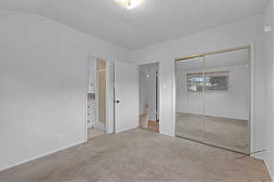 Unfurnished bedroom featuring vaulted ceiling, a closet, and carpet flooring