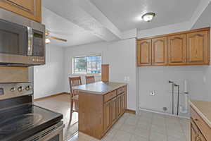 Kitchen with a peninsula, a ceiling fan, light countertops, appliances with stainless steel finishes, and brown cabinets