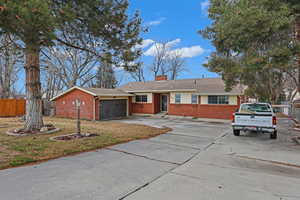 Single story home featuring driveway, a chimney, an attached garage, fence, and brick siding