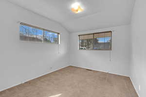 Spare room with carpet, visible vents, vaulted ceiling, and baseboards