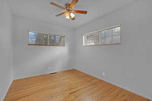 Unfurnished room featuring ceiling fan, wood finished floors, visible vents, and baseboards