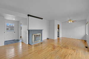 Unfurnished living room featuring hardwood / wood-style flooring, visible vents, baseboards, a ceiling fan, and a brick fireplace