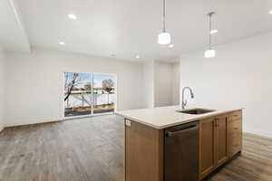 Kitchen featuring dishwasher, open floor plan, decorative light fixtures, light wood-style floors, and a sink