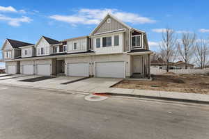 Multi unit property featuring a garage, brick siding, board and batten siding, and concrete driveway