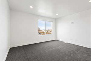 Empty room with dark colored carpet, recessed lighting, and baseboards