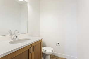 Half bath with wood finished floors, vanity, toilet, and baseboards