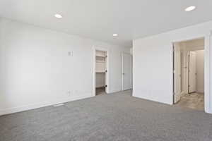 Unfurnished bedroom featuring visible vents, baseboards, a walk in closet, carpet flooring, and recessed lighting