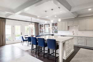 Kitchen featuring coffered ceiling, decorative backsplash, dark wood finished floors, a kitchen breakfast bar, and a center island