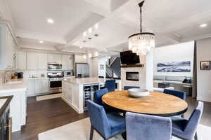 Dining space featuring beam ceiling, dark wood finished floors, a glass covered fireplace, a chandelier, and coffered ceiling