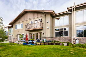 Back of property with a balcony, a yard, stone siding, stucco siding, and board and batten siding