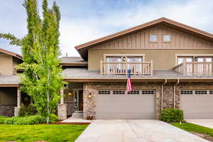 Multi unit property with an attached garage, board and batten siding, a balcony, driveway, and a front lawn