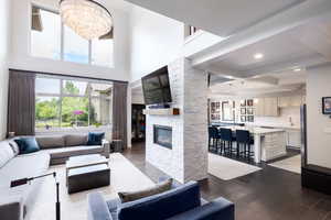 Living room with a high ceiling, dark wood-type flooring, a stone fireplace, a chandelier, and beamed ceiling