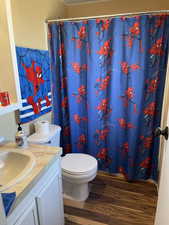 Bathroom with toilet, curtained shower, wood finished floors, and vanity