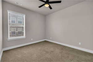 Carpeted spare room featuring a ceiling fan, visible vents, and baseboards