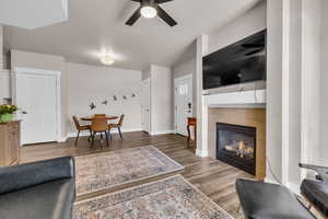 Living room with baseboards, ceiling fan, a tiled fireplace, and wood finished floors