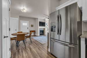 Kitchen featuring baseboards, a glass covered fireplace, ceiling fan, wood finished floors, and stainless steel refrigerator with ice dispenser