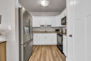 Kitchen featuring white cabinets, light wood-style flooring, light stone counters, black appliances, and a sink