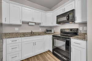 Kitchen with black appliances, light wood finished floors, a sink, and white cabinets