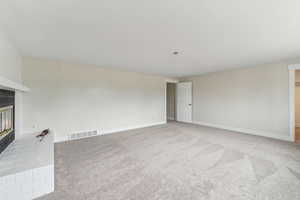 Unfurnished living room featuring light colored carpet and a brick fireplace