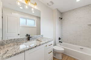 Full bathroom with vanity, toilet, tiled shower / bath combo, and hardwood / wood-style floors