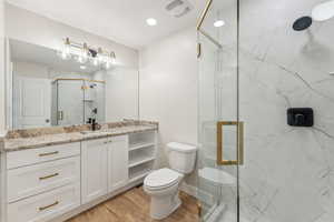 Bathroom featuring wood-type flooring, toilet, vanity, and a shower with shower door