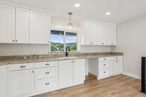 Kitchen featuring decorative light fixtures, light hardwood / wood-style floors, sink, and white cabinets