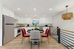 Kitchen with white cabinets, light wood-type flooring, pendant lighting, and stainless steel appliances