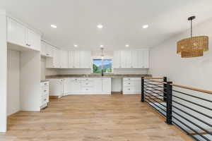 Kitchen featuring stone countertops, sink, white cabinets, hanging light fixtures, and light wood-type flooring