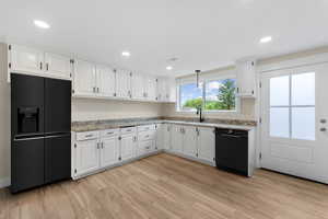 Kitchen with white cabinetry, light hardwood / wood-style flooring, light stone counters, and black appliances