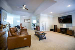 Carpeted living area with a tray ceiling, ornamental molding, a ceiling fan, and baseboards