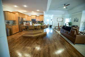 Kitchen featuring dark wood-type flooring, open floor plan, appliances with stainless steel finishes, tasteful backsplash, and crown molding