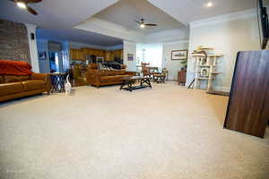 Carpeted living room featuring a tray ceiling, crown molding, baseboards, and ceiling fan