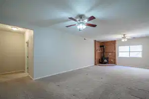 Unfurnished living room with a wood stove, carpet flooring, ceiling fan, and baseboards