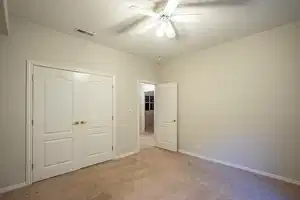 Unfurnished bedroom with light carpet, a ceiling fan, visible vents, and baseboards