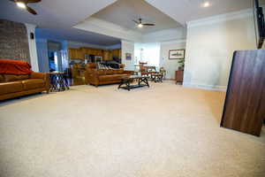 Living room featuring light carpet, baseboards, a ceiling fan, and crown molding