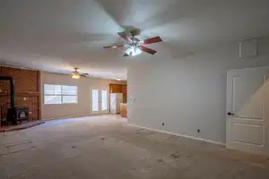 Unfurnished living room with light carpet, baseboards, ceiling fan, a wood stove, and a textured ceiling