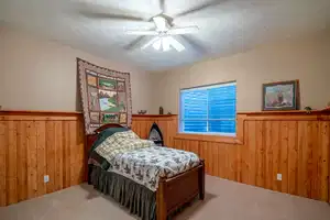 Bedroom with a textured ceiling, wooden walls, a wainscoted wall, a ceiling fan, and carpet