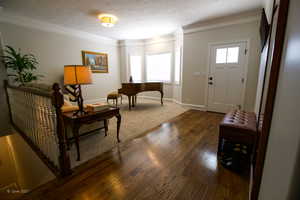 Entrance foyer featuring baseboards, a textured ceiling, ornamental molding, and dark wood-type flooring