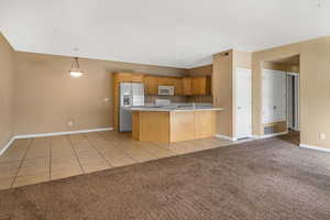 Kitchen featuring white microwave, light tile patterned flooring, light carpet, range, and stainless steel fridge with ice dispenser