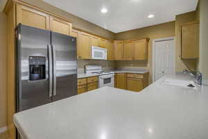 Kitchen with light countertops, white appliances, a sink, and recessed lighting