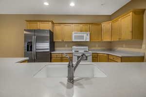 Kitchen with light countertops, white appliances, a sink, and recessed lighting