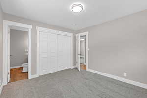 Unfurnished bedroom with carpet floors, a closet, ensuite bath, and baseboards