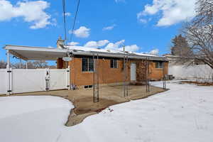 Snow covered house with a patio, a gate, central AC, and brick siding