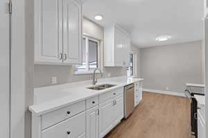 Kitchen featuring light wood-style flooring, appliances with stainless steel finishes, white cabinetry, a sink, and baseboards