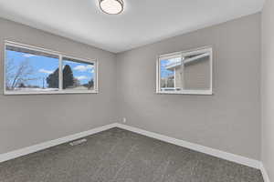 Spare room featuring visible vents, dark carpet, and baseboards