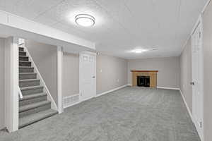 Finished basement featuring visible vents, baseboards, stairway, carpet, and a fireplace